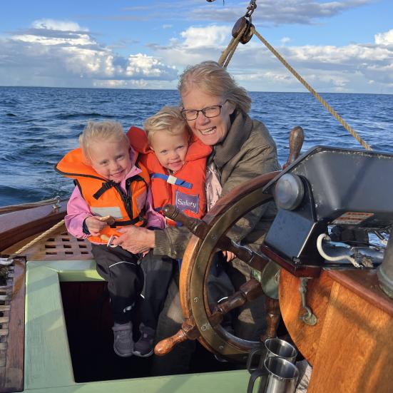 Karen Tilma fotograferet på en båd med 2 børn iklædt redningsveste på skødet