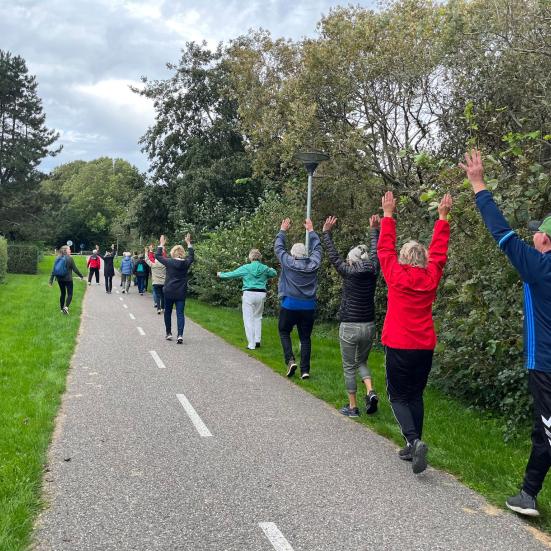En gruppe mennesker, set bagfra, går i vejsiden med hænderne over hovedet.