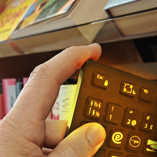 Nærbillede af hånd, der trækker et computertastatur ud mellem bøgerne på en hylde. Flere af tastaturets knapper er udskiftet med logoer for eReolen, Filmstriben etc..