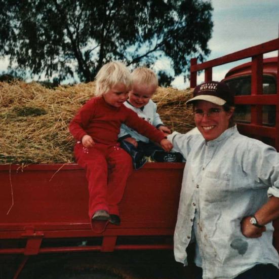 Rikke Nesbit i arbejdstøjet står ved en lastbil fyldt med halm. I halmen sidder 2 yngre børn.