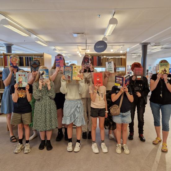 Børn der holder bøger med forsiden fremad foran deres ansigter