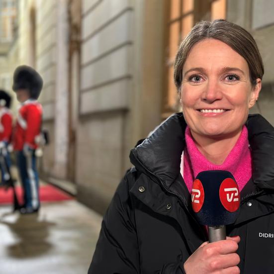 Foto af Marie Rønde foran Amalienborg. To gardere skimtes i baggrunden.n