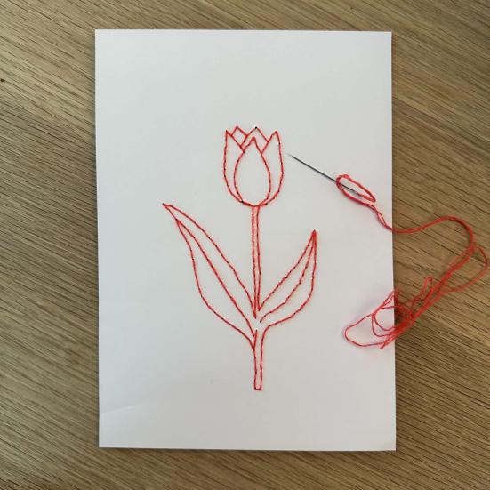 Et ark papir med en broderet blomst samt et synål med rød tråd