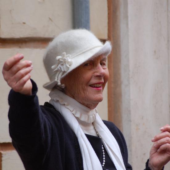 Kvindelig senior med hvid filt hat rækker ud og smiler.