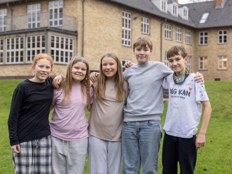 5 børn står med armene på hinandens skuldre foran Julemærkehjemmet