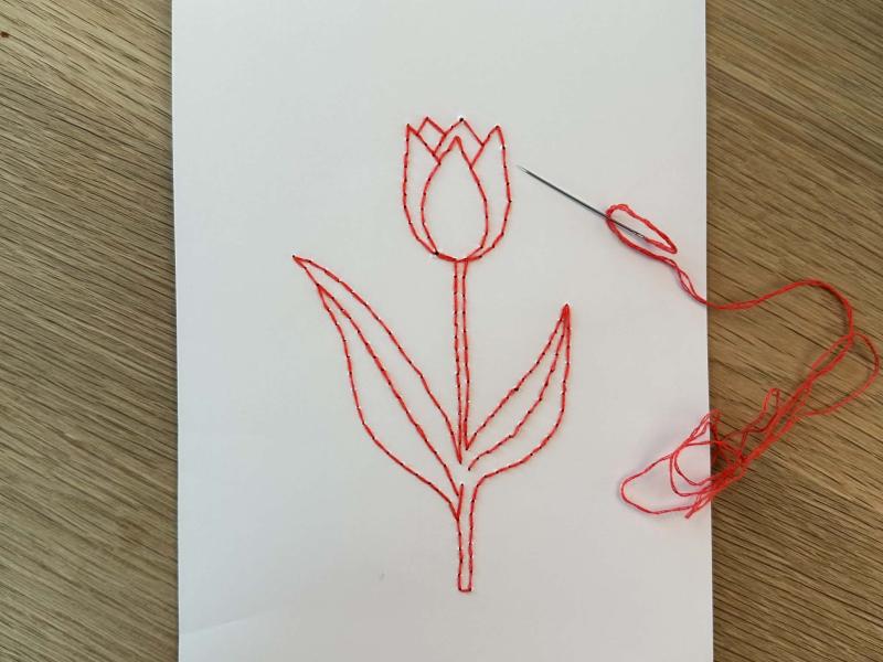 Et ark papir med en broderet blomst samt et synål med rød tråd