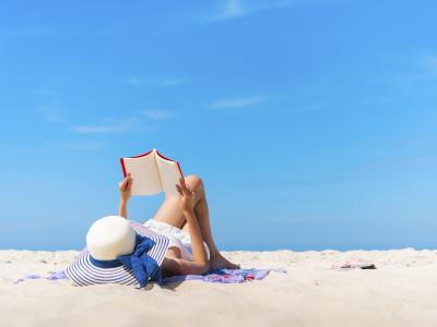 Kvinde ligger på en eksotisk strand og læser