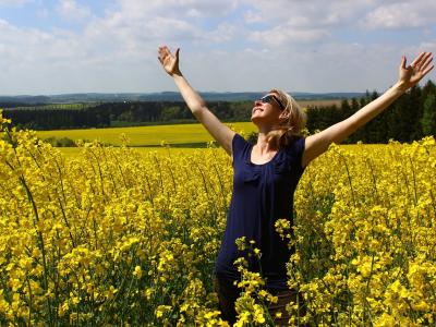 Kvinde står i rapsmark og løfter armene mod himmelen