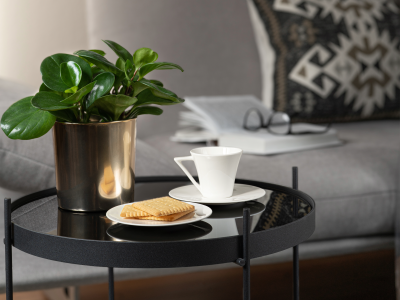 Et sofabord med kaffe og kiks. I baggrunden en opslået bog på en sofa