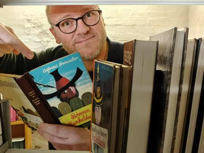 Biblioteksformidler Hans Wendelboe Bøcher med børnebogen "Røveren Runkeldunk", set gennem magasinets bogreoler.