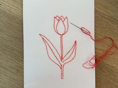 Et ark papir med en broderet blomst samt et synål med rød tråd