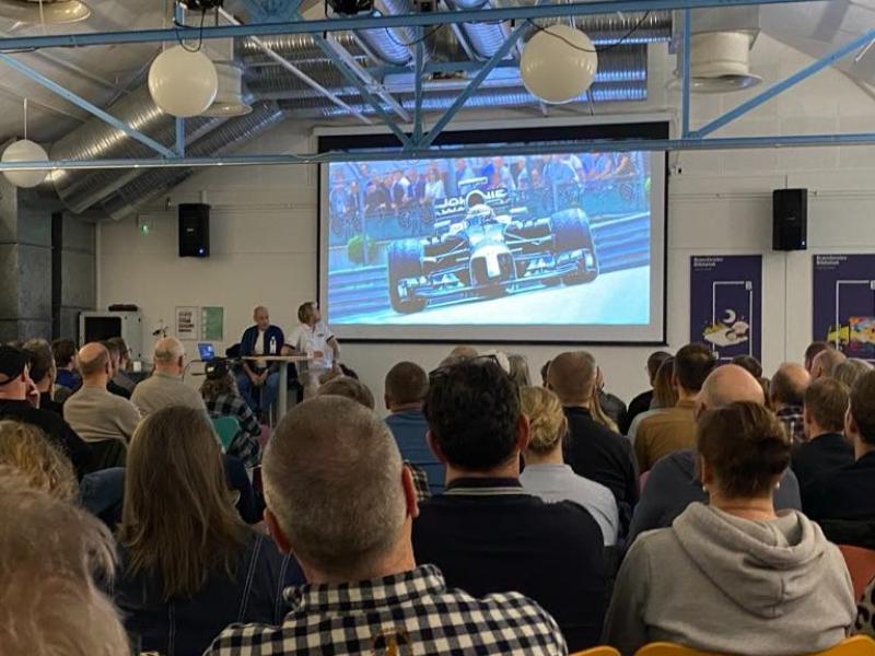 Publikum i salen på Brønderslev Bibliotek, set bagfra. På lærredet ses en formel1-racer.l1-arrangement 2025