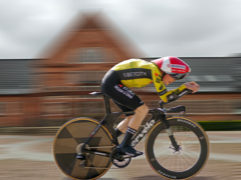 Jonas Vingegaard i gul førertrøje sprinter forbi Brønderslev Bibliotek, der ses sløret i baggrunden. Fotocollage. 