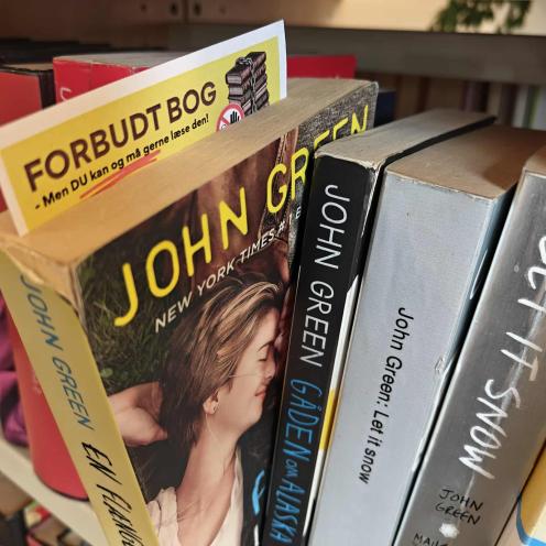 Gul seddel med teksten "Forbudt bog", stukket ned i John Greens 'En flænge i himlen'
