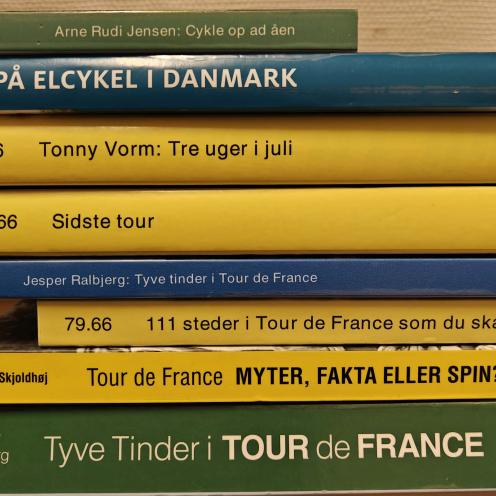 Stak af bogrygge, der alle handler om profesionel cykling, Tour de France eller danske cykelruter.