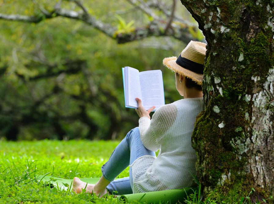 Kvinde læser en bog i skyggen under et træ