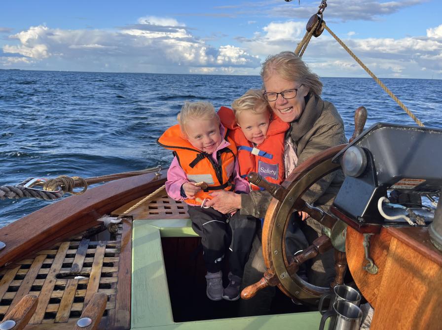 Karen Tilma fotograferet på en båd med 2 børn iklædt redningsveste på skødet