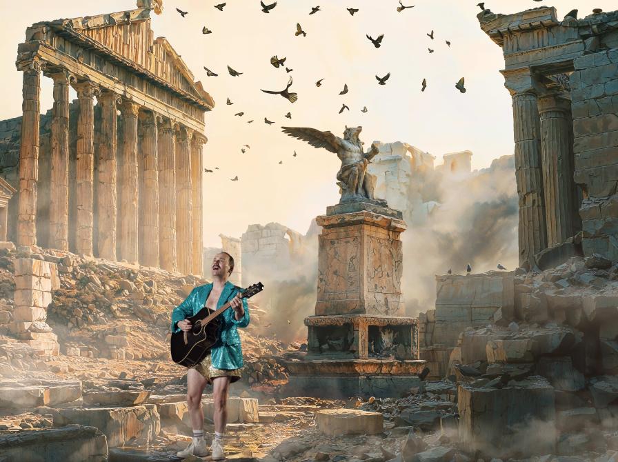 Mand i turkis jakke spiller guitar midt i græske ruiner