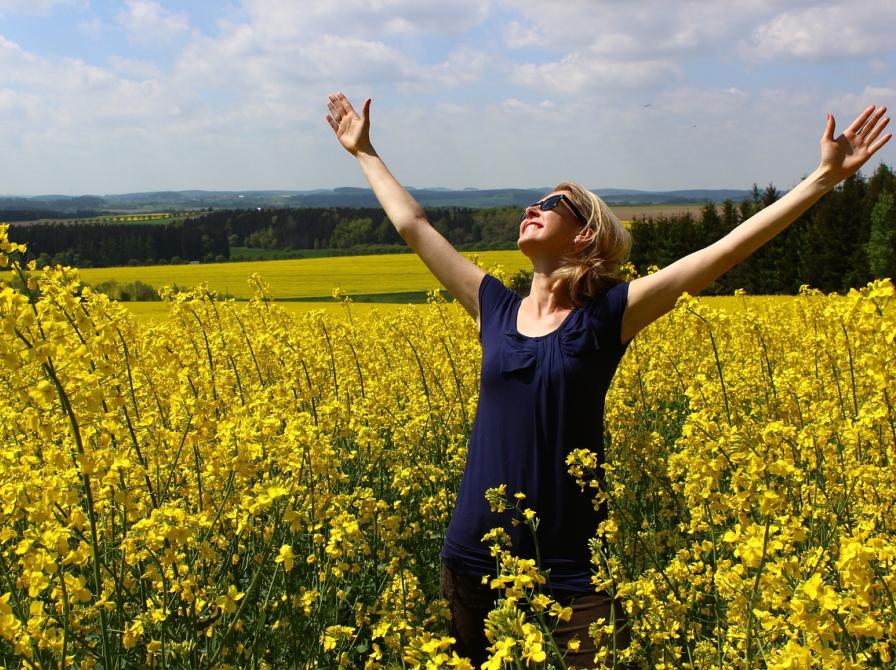 Kvinde står i rapsmark og løfter armene mod himmelen