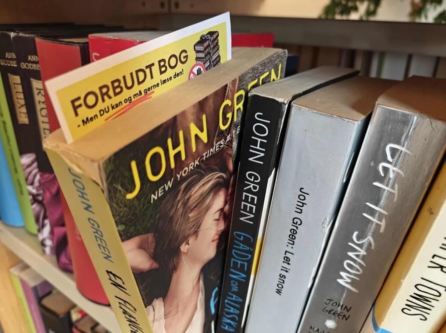 Gul seddel med teksten "Forbudt bog", stukket ned i John Greens 'En flænge i himlen'