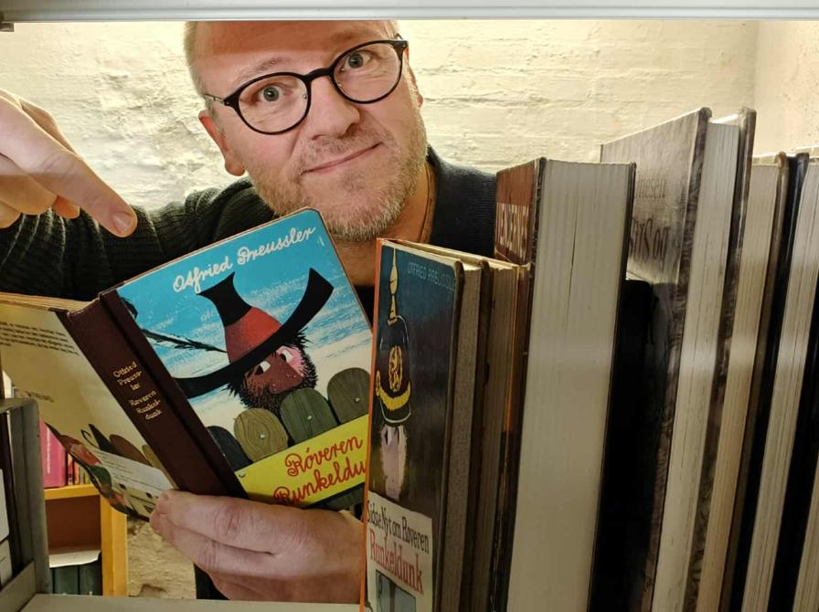 Biblioteksformidler Hans Wendelboe Bøcher med børnebogen "Røveren Runkeldunk", set gennem magasinets bogreoler.