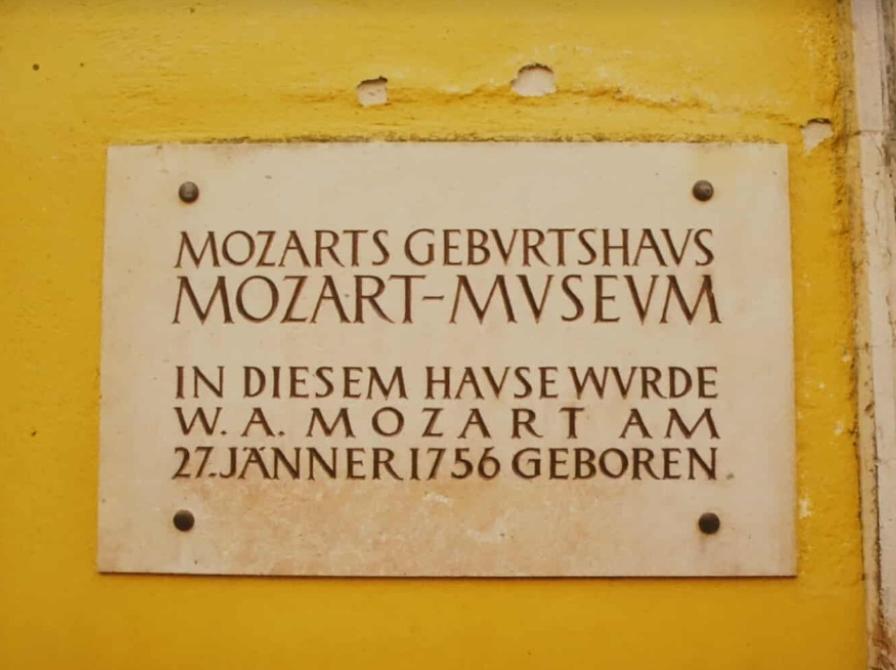 Foto af hvid mindeplade på den gule husfacade på Mozarts fødehjem i Salzburg.