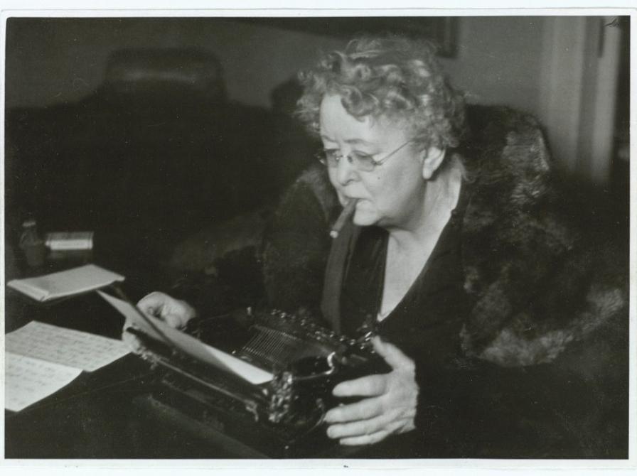 Thit Jensen med cigar i mundvigen sidder ved sin skrivemaskine. Sort/hvidt foto.