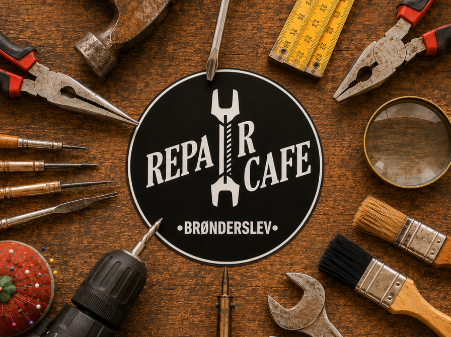 Repair Café Brønderslevs runde logo, omgivet af forskelligt håndværktøj på en slidt træbordplade.